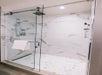 Glass shower with marble tile walls, a rainfall showerhead, and a towel hanging on the door.