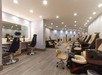 A modern, well-lit salon interior with multiple pedicure stations, a long mirror with chairs, and gray wood flooring.
