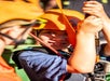 Close up of a young person wearing an orange helmet and smiling while holding onto the ropes of their zip line harness.
