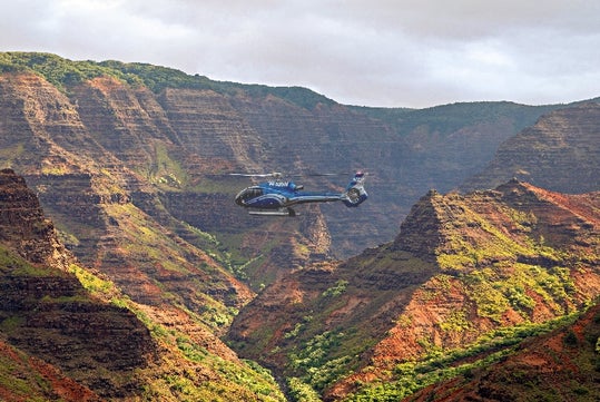 A helicopter flying by a red-colored mountain range on the Kauai Eco Adventure Helicopter Tour in Hawaii USA.