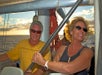 A smiling couple enjoys the ocean breeze aboard a Na Pali Coast sunset cruise, with the sun setting behind them.