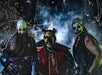 Three people in eerie clown costumes and face paint stand together at night, with a foggy background and dark, dramatic lighting.