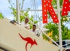 Two people enjoy a roller coaster ride. The older man and young boy are smiling and seated in a car with a red kangaroo logo. Trees and a "K" sign are in the background.