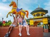 Three teenagers snapping a selfie while seated on a brick wall next to a horse carousel figure at the entrance to Kennywood.