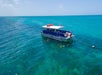 A group of people swim near a boat anchored in clear turquoise ocean water under a blue sky.