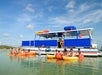 People in kayaks are gathered near a blue and white boat on calm water under a partly cloudy sky.