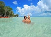 Two people wearing snorkel gear stand in clear, shallow water with a canoe and trees visible in the background.