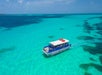 A blue and white boat travels across clear turquoise water under a blue sky.