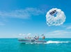 Boat with passengers towing a person in a white parasail labeled "Fury" over clear blue water.