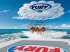 Three people are parasailing over the ocean, attached to a boat with "Fury" branding. The sky is clear with a few clouds.