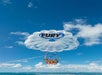 Two people parasailing over the ocean under a white parachute with "Fury" written on it, set against a clear blue sky.