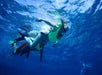 Two people snorkeling underwater with clear visibility, wearing flippers and snorkel masks in a vibrant blue sea.