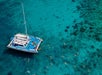 Aerial view of a catamaran anchored in clear turquoise water, surrounded by people snorkeling.