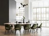 A modern dining room with a large marble table surrounded by green velvet chairs. A black chandelier hangs above, and the room features large windows and wooden flooring.