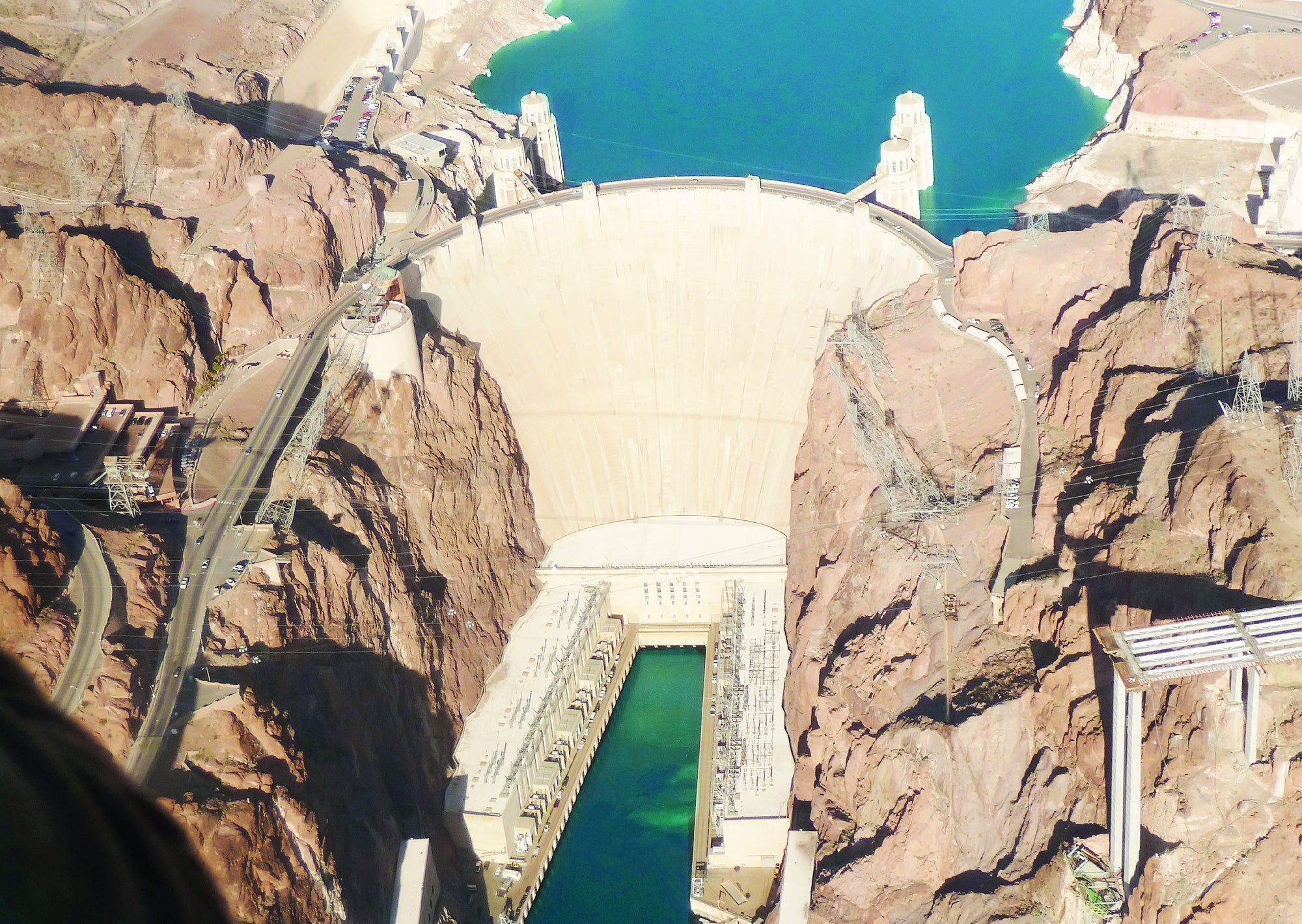 Aerial view of a large dam with water reservoirs on both sides, surrounded by rocky terrain.
