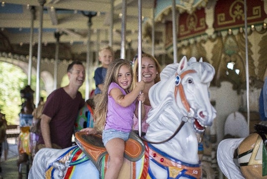 A mother and her young daughter riding a carousel together and laughing at Kings Dominion in Doswell, Virginia.