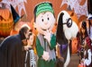 People in Halloween costumes, including children and adults, stand with characters dressed as Frankenstein and a dog in front of pumpkins and spider web decorations.