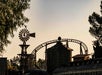 A wooden windmill, water tower, and roller coaster track are silhouetted against the evening sky, with trees framing the scene.