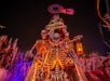 Three large skeleton figures are posed in front of a "Knott's Scary Farm" sign at night, surrounded by spooky decorations and eerie lighting.