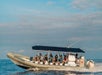 A super- raft full of people sailing through the water with the sun shining down on them and clouds in the sky behind them.