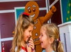 Two young girls laughing together with a large gingerbread character in the background.