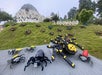 A colorful Lego scene at Legowood, featuring a variety of large Lego spiders on a grassy hill, with a whimsical building in the background and the "LEGOWOOD" sign prominently displayed.
