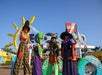 Four people in colorful witch costumes stand in front of a LEGOLAND sign decorated with Halloween-themed LEGO structures under a clear blue sky.