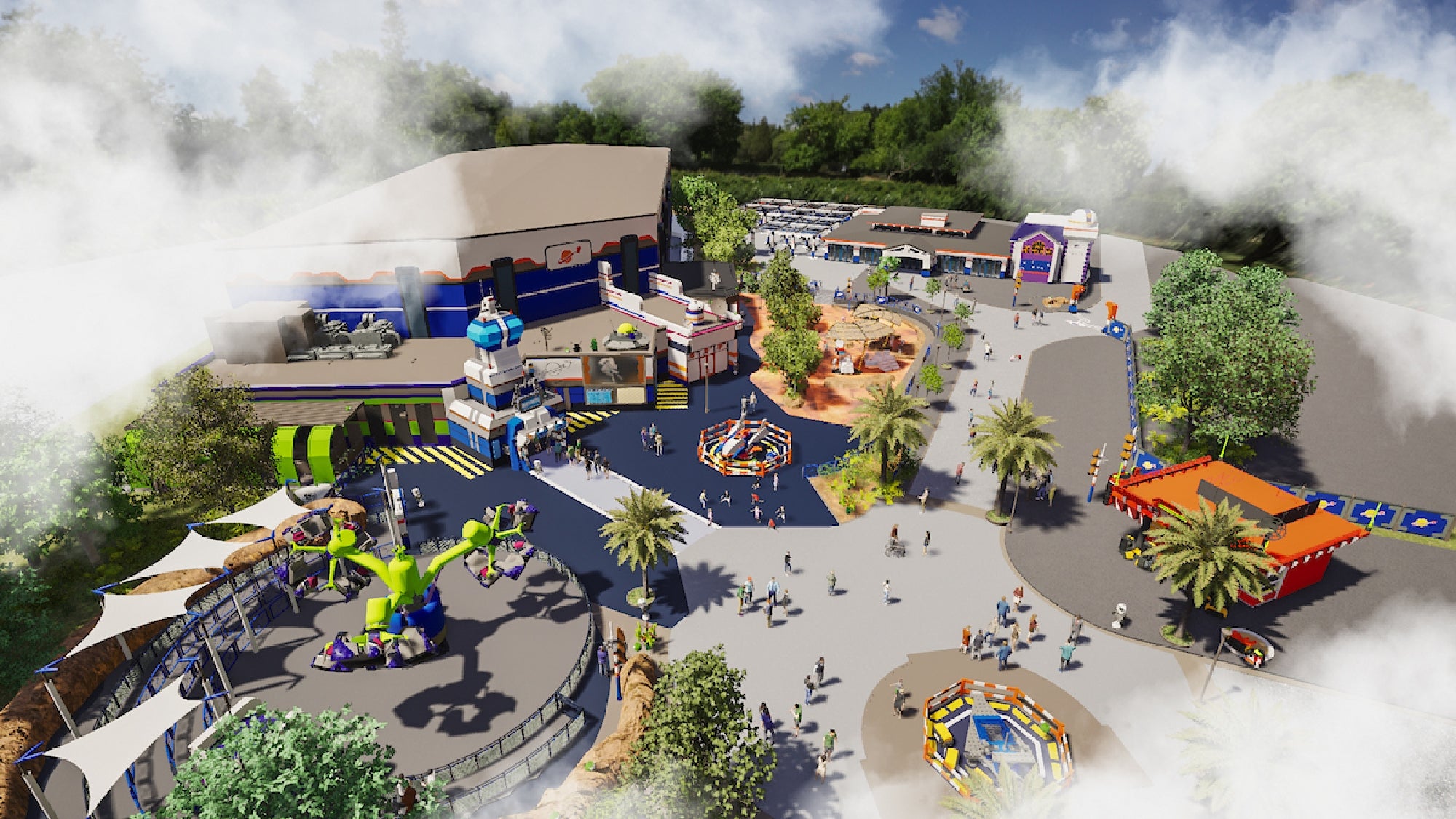 Aerial view of an amusement park area with various rides, colorful buildings, palm trees, and scattered visitors under a partly cloudy sky.