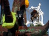 LEGO sculptures of a black bear, green snake, and large spider on a white web are displayed on a tree-like structure against a blue sky.