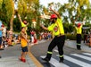 A young boy high-fives a performer in a neon safety outfit and red hard hat during an outdoor event with people watching in the background.