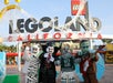 Four people in LEGO monster costumes pose in front of the LEGOLAND California entrance decorated with spider webs.
