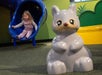A young girl slides down a blue playground slide while a large gray animal statue is positioned in the foreground.