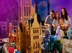 A family of four observes a detailed LEGO model of Big Ben and other buildings, with Halloween-themed LEGO decorations in the scene.