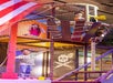 Three children play in a pirate-themed indoor playground structure, featuring a climbing area and a flag with a skull and crossbones.
