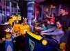 A family of four rides in a Lego-themed amusement park attraction, aiming toy guns at targets in a medieval treasure room setting.