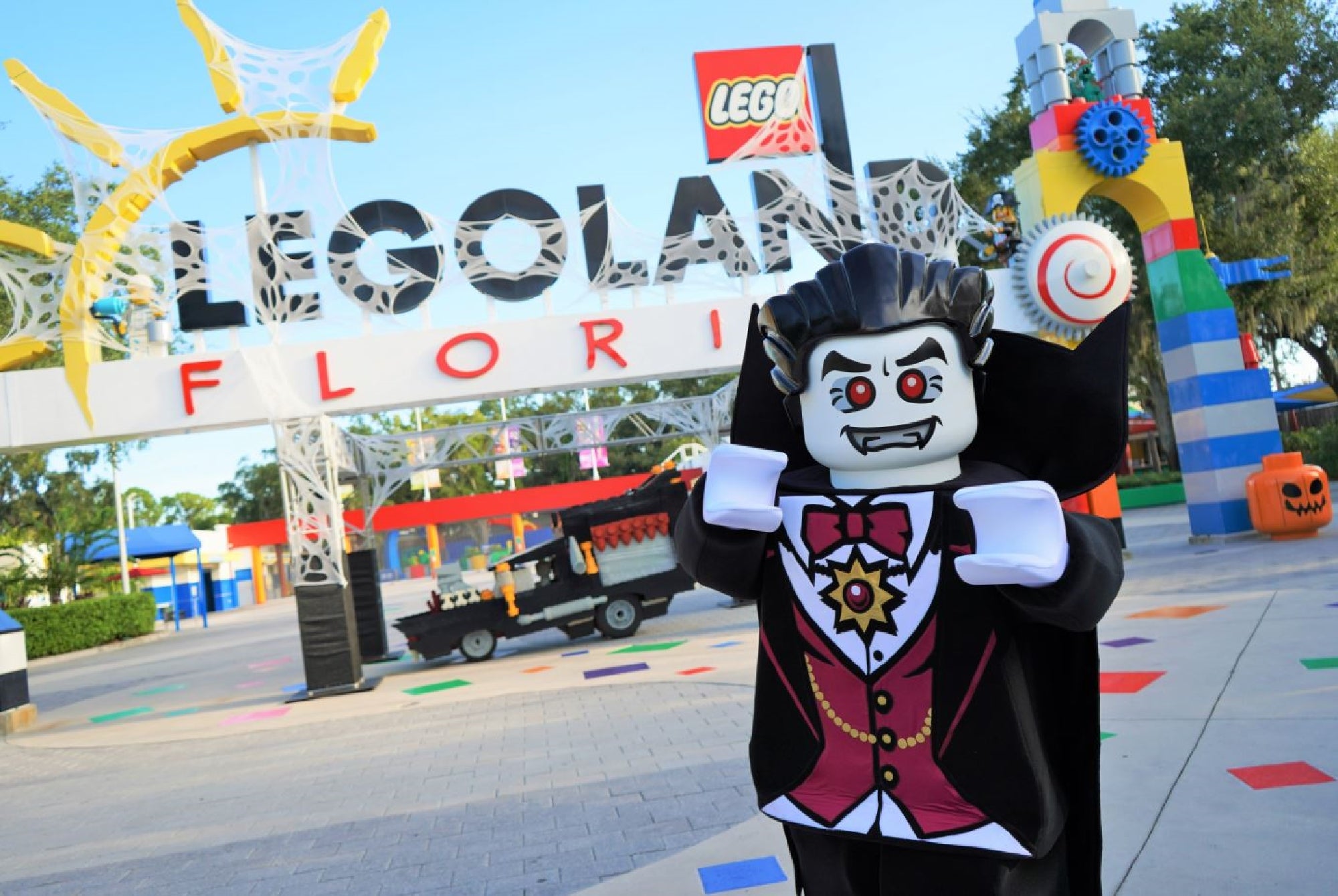 A person in a vampire LEGO costume poses in front of the entrance sign to LEGOLAND Florida, decorated with Halloween props.