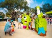 A man takes a photo of two children standing beside large, colorful LEGO sculptures outdoors on a sunny day.