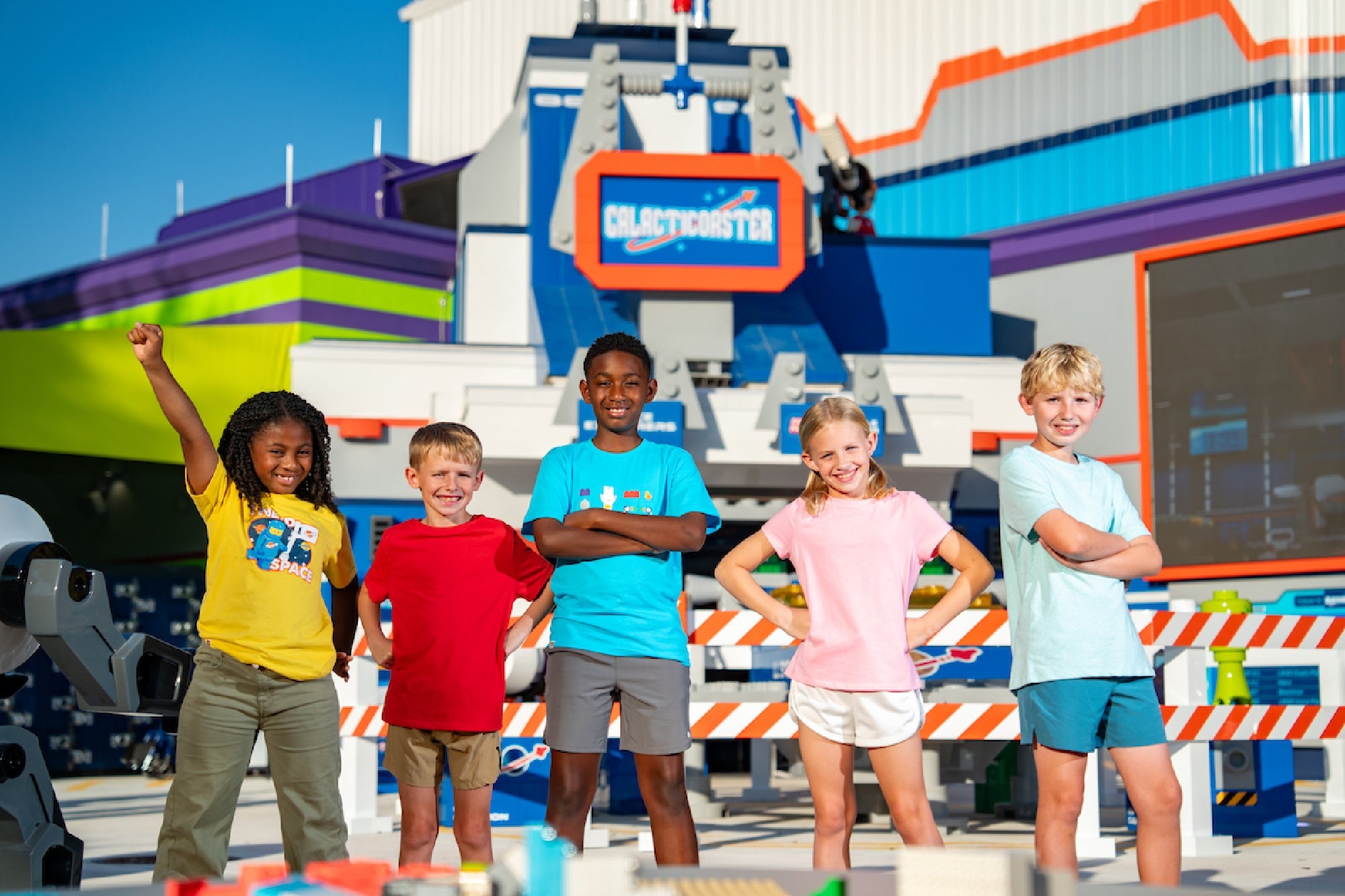 Five children stand smiling in front of a colorful outdoor attraction with the sign "Collection Center" and playful building block decorations.