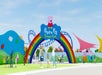 Entrance to Peppa Pig Theme Park featuring a rainbow arch, colorful decorations, and visitors walking nearby under a clear blue sky.