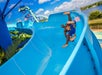Two children joyfully sliding down a bright blue water slide, surrounded by a sunny atmosphere and lush greenery.