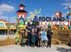 A group of children in costumes pose with a person in a witch costume at LEGOLAND New York, surrounded by Halloween decorations and hay bales.