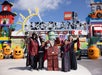 A group of people in Halloween costumes pose with a Frankenstein LEGO character at LEGOLAND, surrounded by pumpkin decorations and colorful LEGO structures.