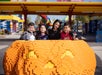 A woman and three children stand behind a large LEGO pumpkin at an outdoor amusement park decorated with colorful LEGO structures.