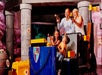 Two parents and two children sitting in a medieval themed ride that looks like its made of LEGO holding laser guns and laughing.