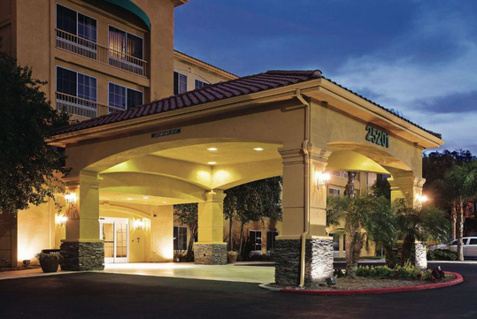 A hotel entrance with a covered driveway, illuminated at dusk. Palm trees and a parked car are visible.