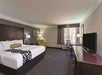 Hotel room with a king-size bed, TV, desk, chair, and armchair. Neutral-toned decor with a window offering natural light.