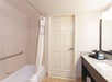 Bathroom with a bathtub and shower curtain, a wooden door, a granite countertop with a mirror, and a coffee maker on the right.