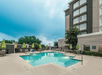 Outdoor hotel pool with lounge chairs, green umbrellas, and a multistory building in the background.