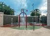 A small water play area with a red arch sprinkler, a water-dumping bucket, and a palm tree-shaped sprayer on a wet surface.