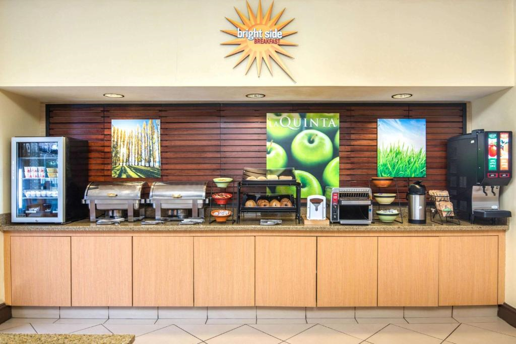 A hotel breakfast area with a counter displaying chafing dishes, a bread rack, a toaster, coffee dispensers, and a juice machine. Signs above feature nature images and the words "bright side breakfast.